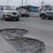Pothole filled urban street with cars driving around a large crater dominates the road surface on a busy avenue   Informe Regio