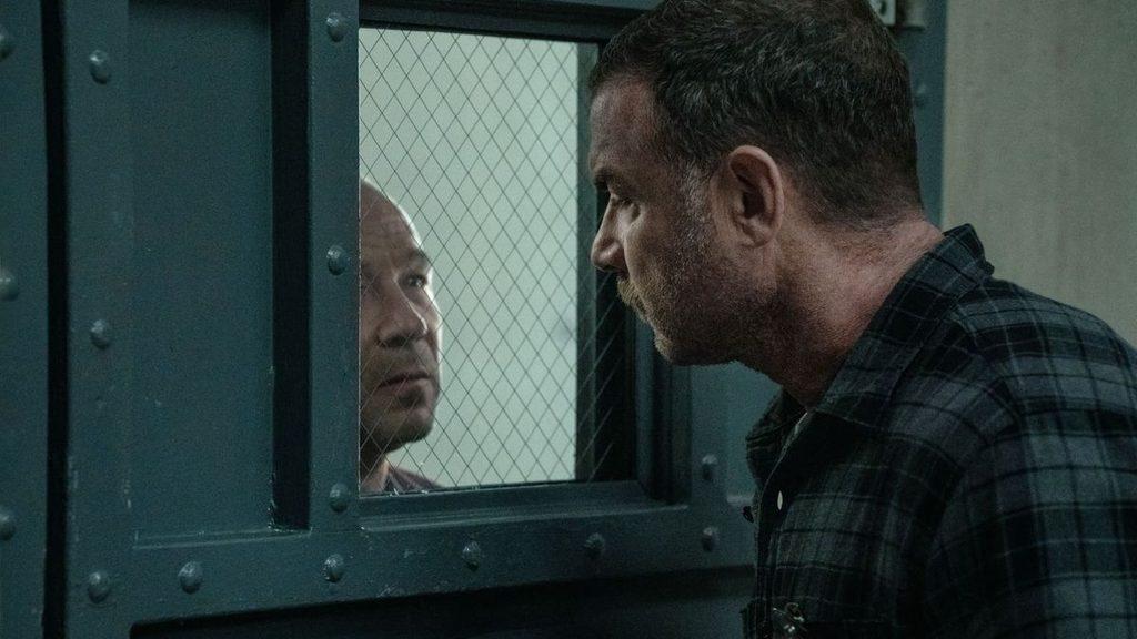 A man in a dark plaid shirt leans in to talk through a jail cell window to an inmate on the other side separated by mesh glass and metal frame   Informe Regio