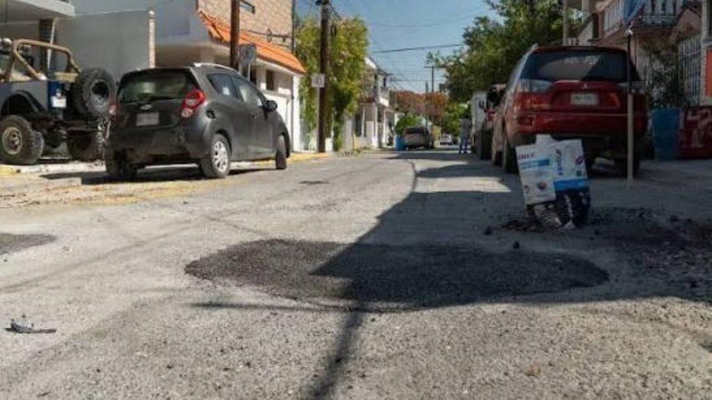 Residential street with parked cars on both sides and fresh asphalt patches filling potholes under a sunny sky   Informe Regio