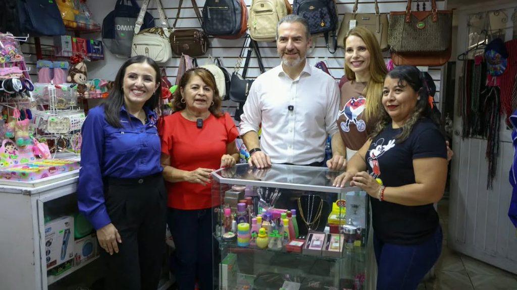 Five smiling adults stand around a glass display case in a store filled with handbags and toys posing for a group photo   Informe Regio