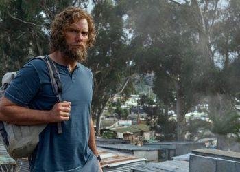 Informe-regio-prime-video-chris-pratt-la-terminaljpg - Informe Regio Bearded man in a blue shirt with a gray backpack stands in a cluttered outdoor area with trees and makeshift buildings ahead Informe Regio