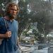Bearded man in a blue shirt with a gray backpack stands in a cluttered outdoor area with trees and makeshift buildings ahead   Informe Regio