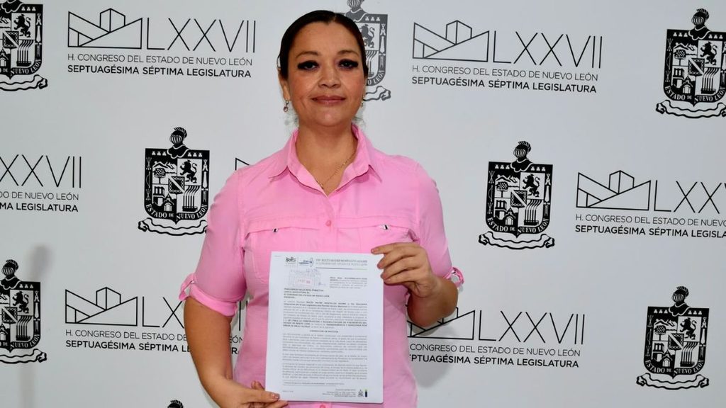 Woman in a pink shirt holding a document posing in front of a backdrop featuring H Congreso del Estado de Nuevo León logos   Informe Regio