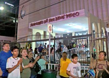 Crowd lines up outside a religious shrine at night, behind a decorative gate and a storefront sign that reads 'Antiguorio de San Judas Tadeo'.