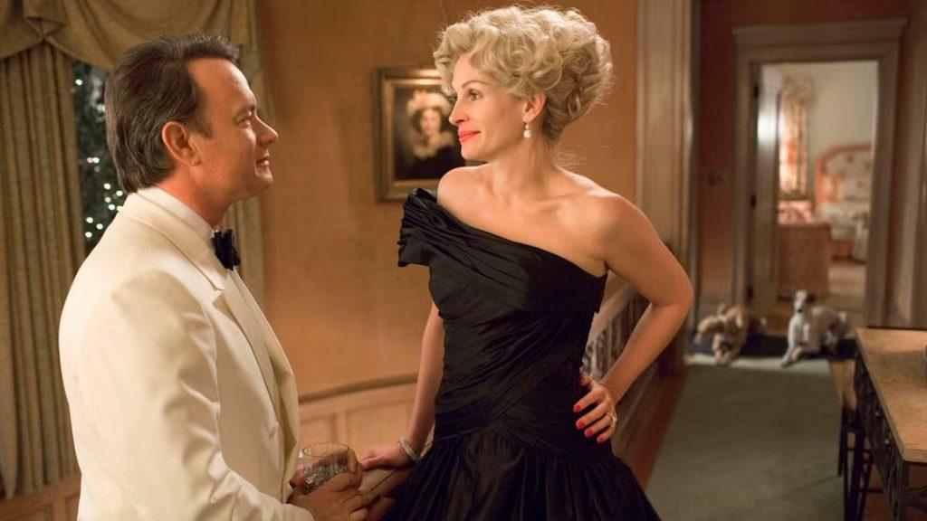 Man in a white tuxedo and a woman in a black off shoulder gown converse in a warmly lit hallway holding drinks   Informe Regio